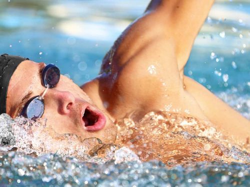 A man with goggles and a swim cap swimming laps in a pool